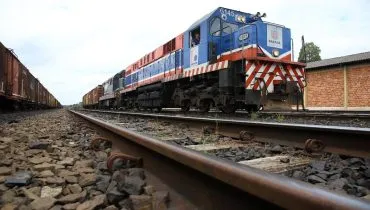 Imagem mostra um trem azul em uma ferrovia, com detalhe para a linha que percorre grande parte da imagem com o trem ao fundo.