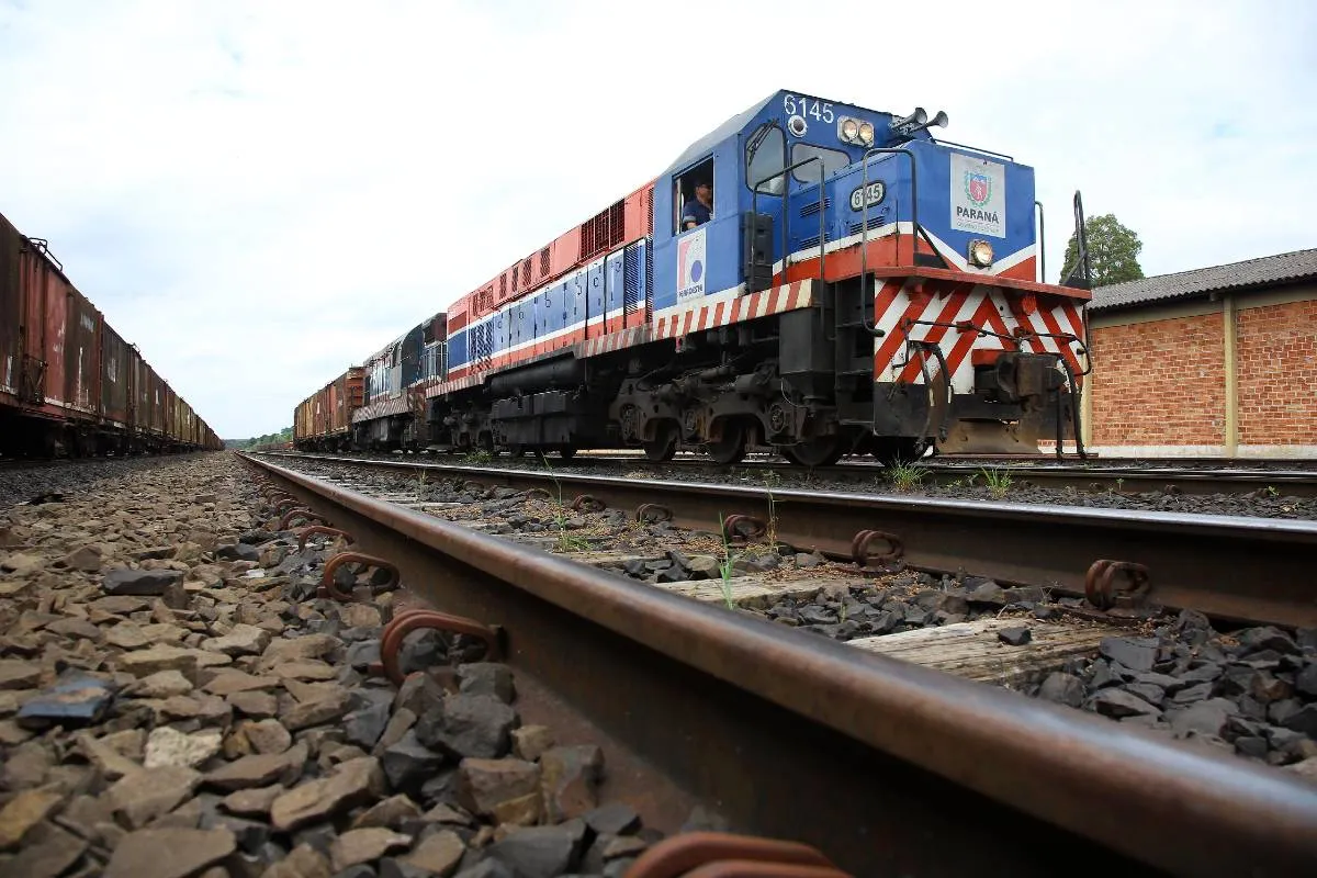 Imagem mostra um trem azul em uma ferrovia, com detalhe para a linha que percorre grande parte da imagem com o trem ao fundo.