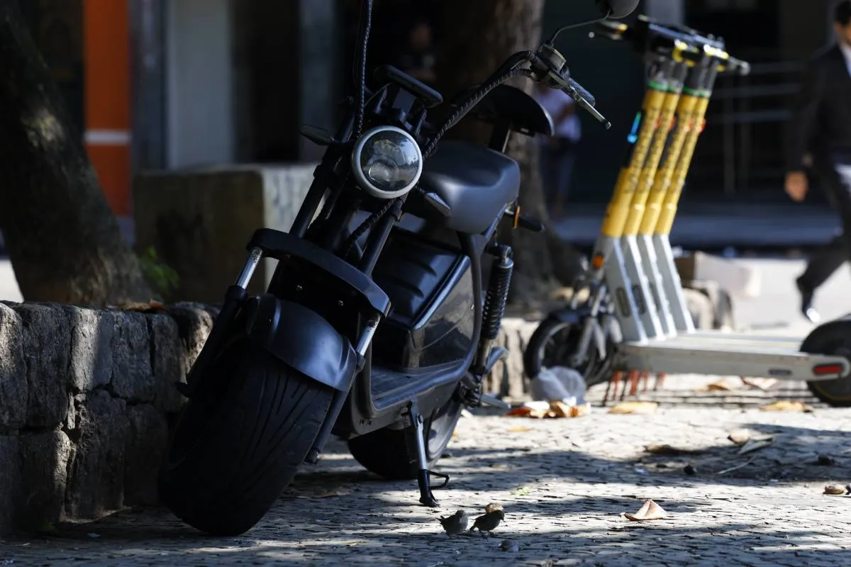Imagem mostra uma moto elétrica estacionada em uma calçada de praia.