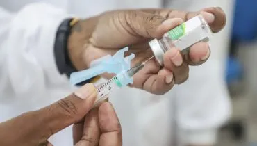 Imagem mostra mãos de uma funcionário de posto de saúde abastecendo uma seringa com a vacina da gripe