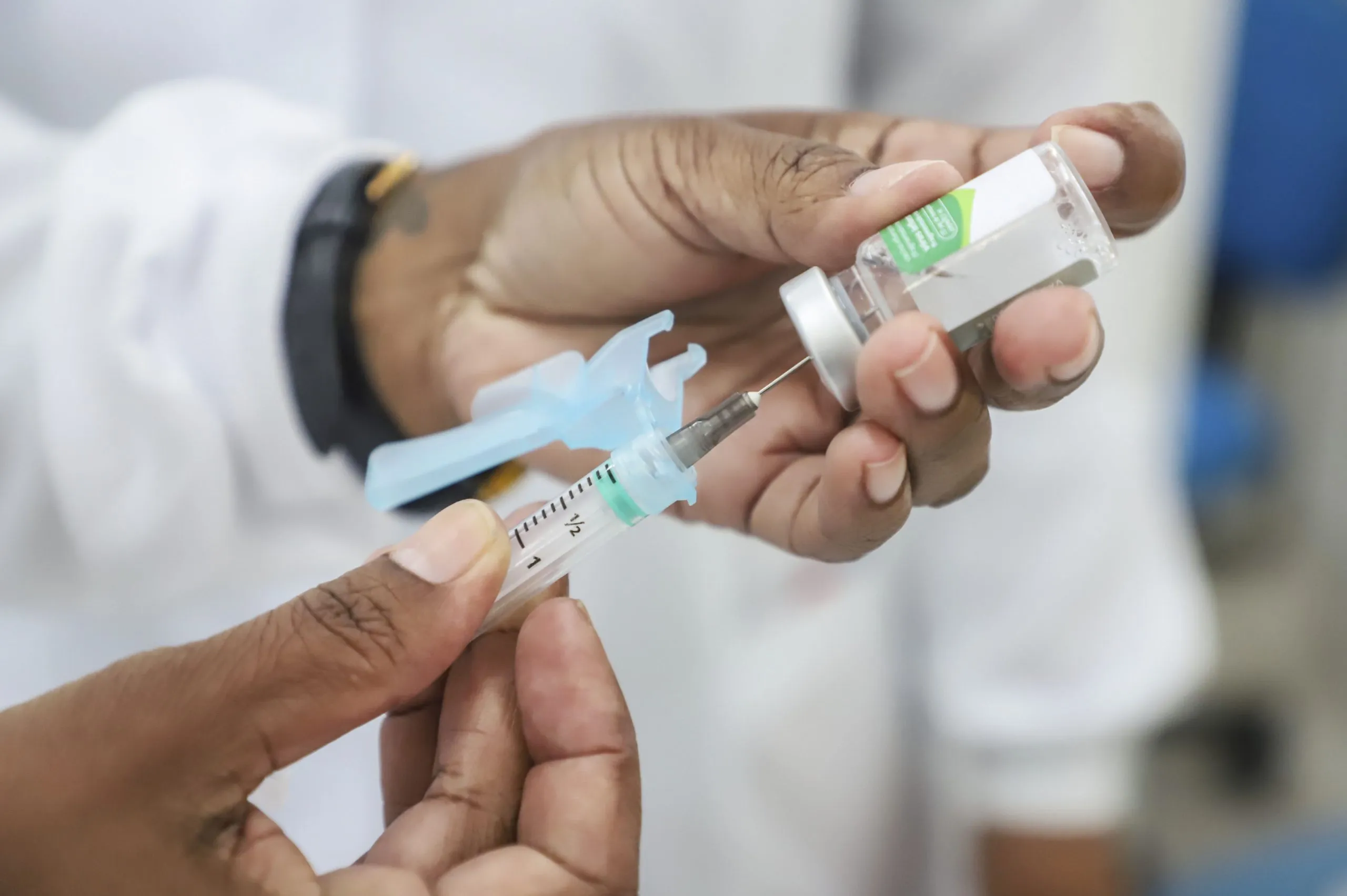 Imagem mostra mãos de uma funcionário de posto de saúde abastecendo uma seringa com a vacina da gripe