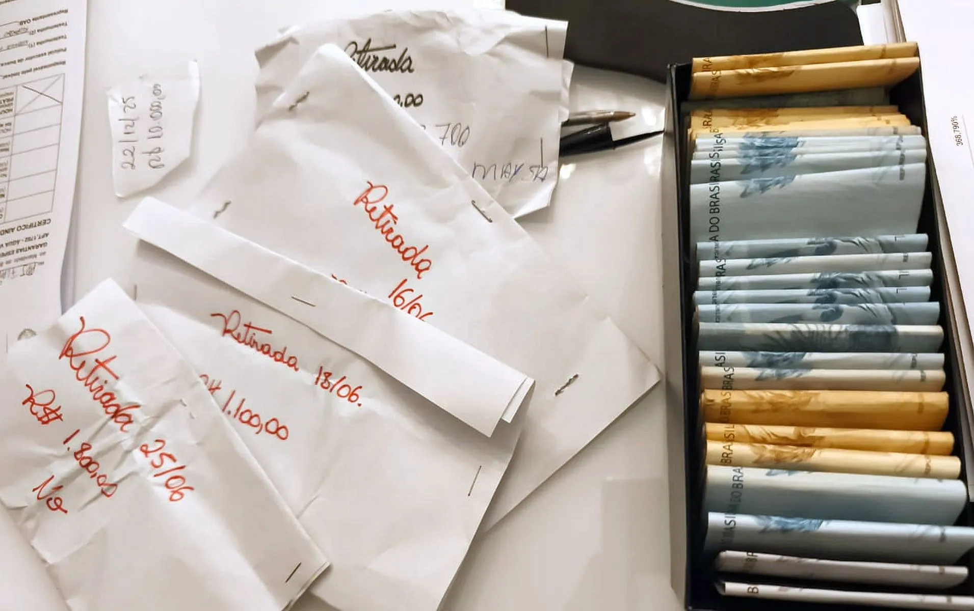 Imagem mostra dinheiro dentro de uma caixa, organizados por favores, e envelopes com valores descritos
