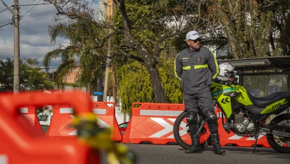 Imagem mostra um agente de trânsito ao lado de uma moto e cones de sinalização em Curitiba.