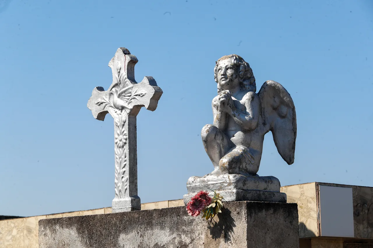 Imagem mostra uma cruz eu um anjo em cima de um túmulo