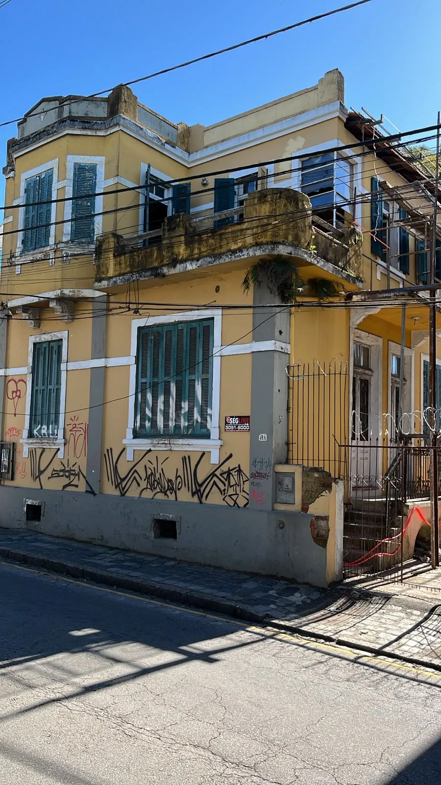 Antiga fachada da Casa Maleski, uma casa antiga no centro histórico de Curitiba. Fachada em amarelo, toda estragada, pichada e tomada por mato em uma sacada