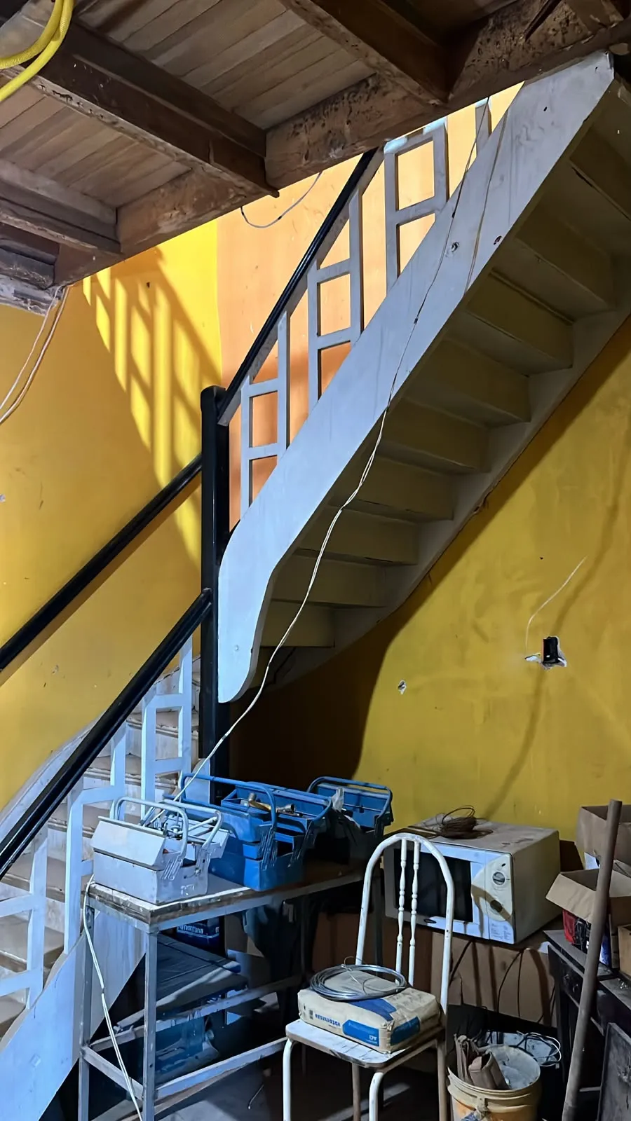 Materiais de obra guardados embaixo de escada de madeira antiga na Casa Maleski