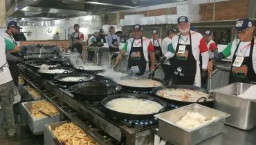 imagem mostra voluntários fritando frango e polenta em vários tachos em um fogão gigante