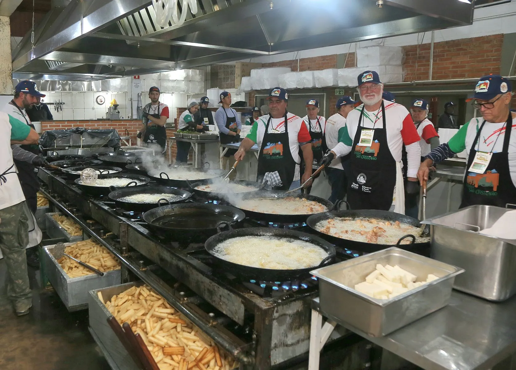 imagem mostra voluntários fritando frango e polenta em vários tachos em um fogão gigante