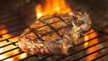 Imagem mostra uma carne sendo grelhada na churrasqueira.