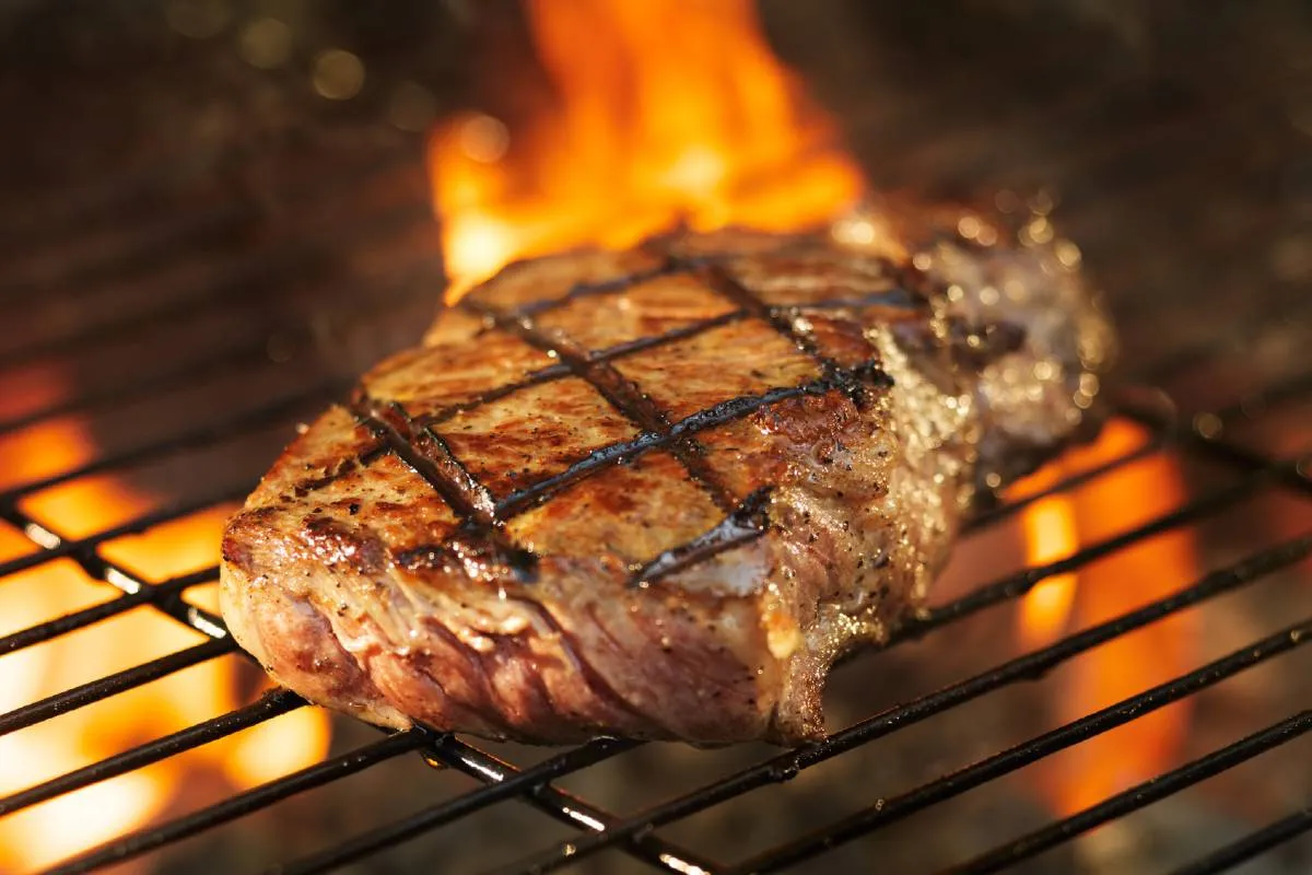 Imagem mostra uma carne sendo grelhada na churrasqueira.