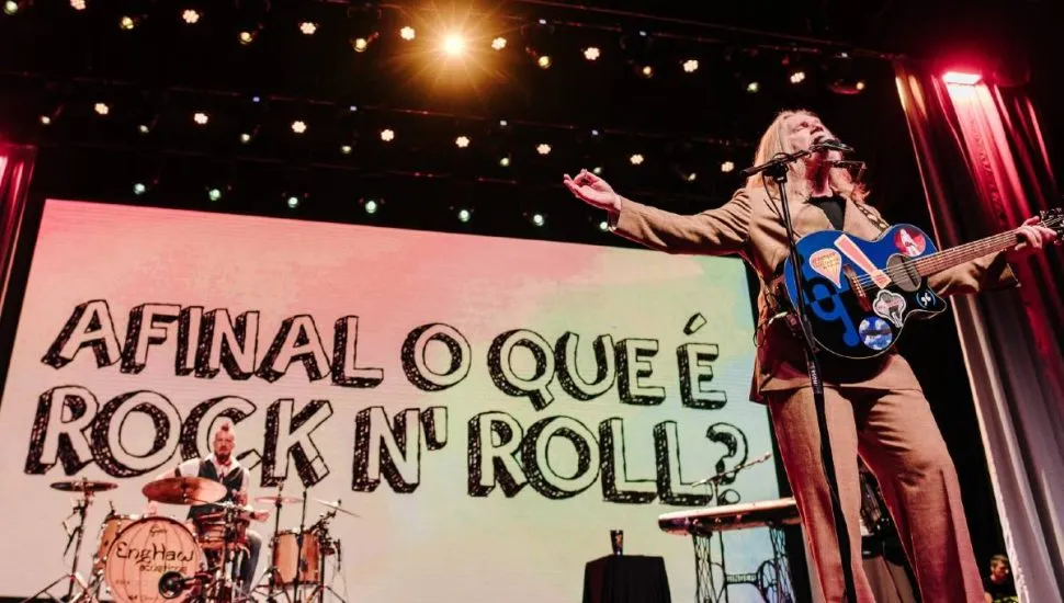 Imagem mostra Humberto Gessinger no palco com a frase ao fundo: Afinal, o que é Rock n´ Roll?