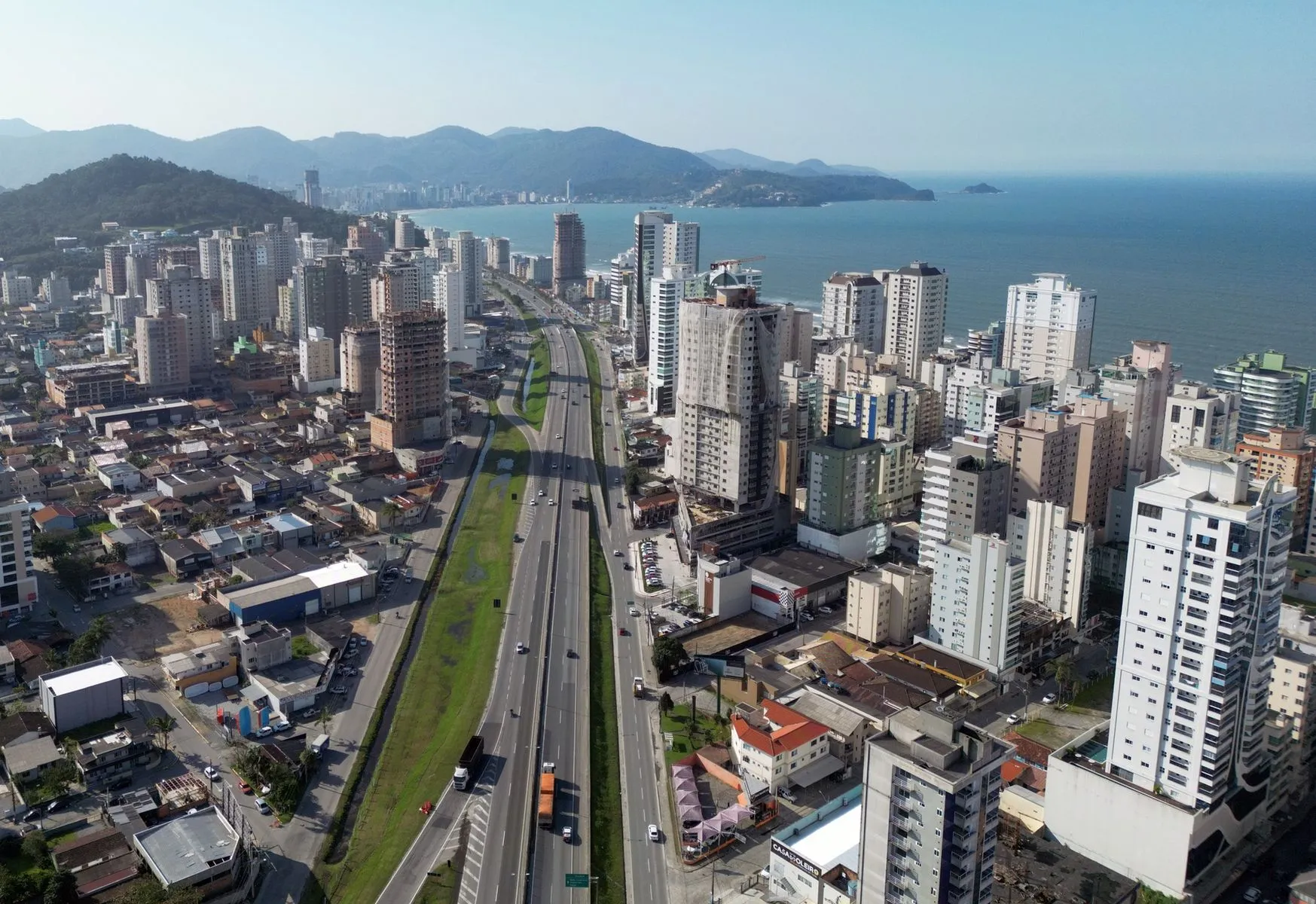 Foto aérea mostra BR-101 no centro da imagem, com prédios dos dois lados e o mar ao fundo