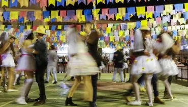 salão decorado com bandeirolas de festa junina tem vários casais caracterizados como caipiras dançando