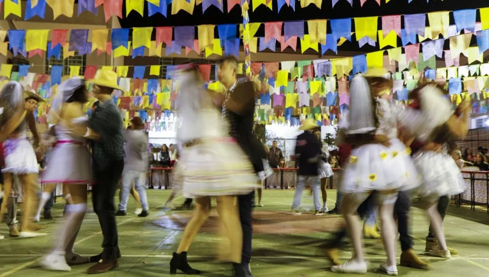 salão decorado com bandeirolas de festa junina tem vários casais caracterizados como caipiras dançando