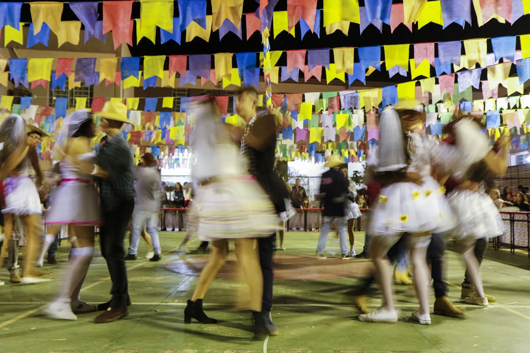 salão decorado com bandeirolas de festa junina tem vários casais caracterizados como caipiras dançando