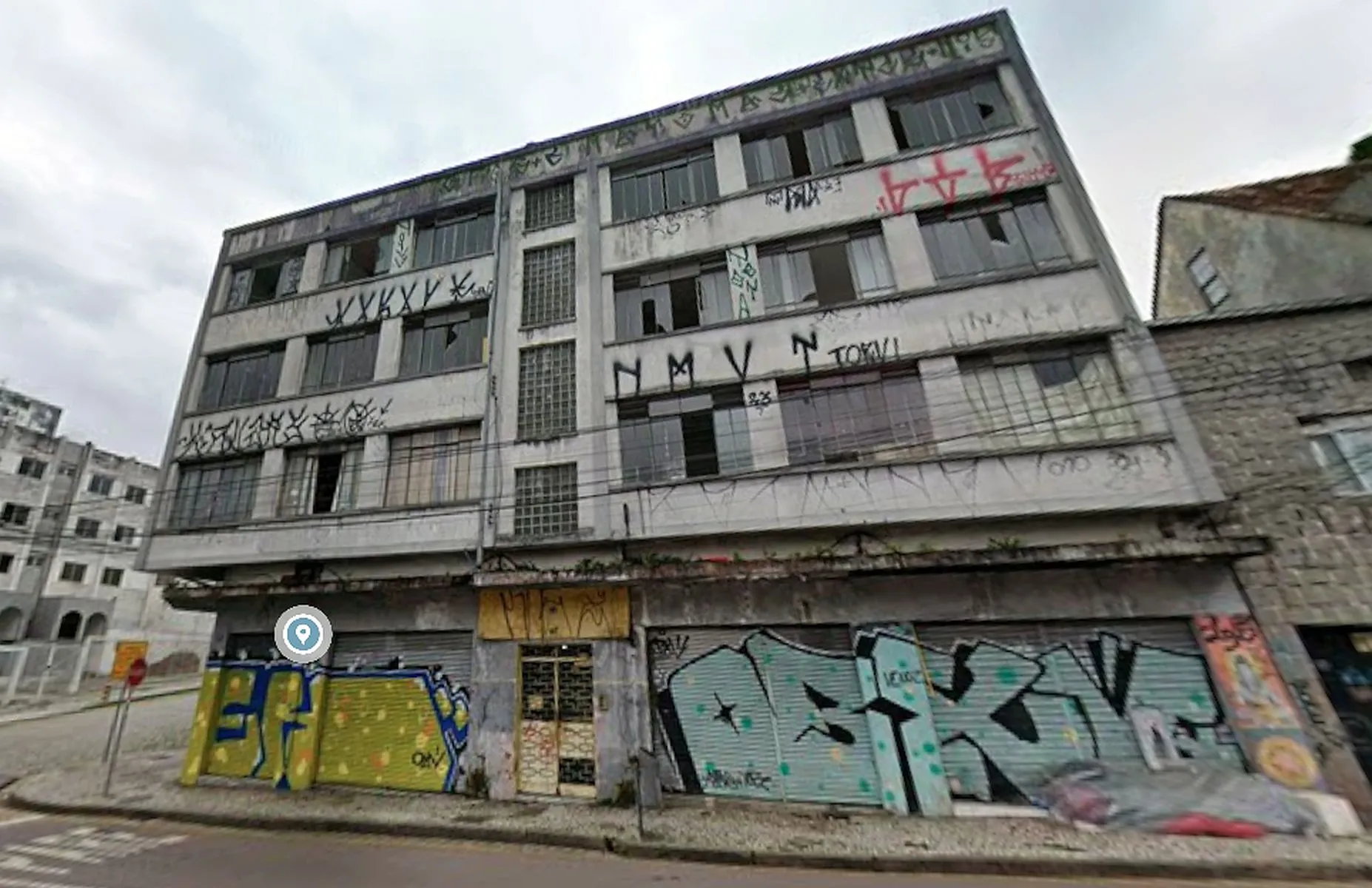 Imagem mostra um prédio de três andares totalmente vandalizado, com vidros quebrados e paredes pichadas