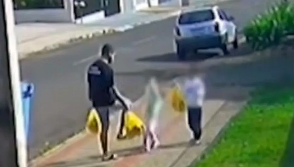 Imagem mostra homem carregado com sacolas de mercado chutando a filha, que também carregada uma sacola, ao lado do irmão