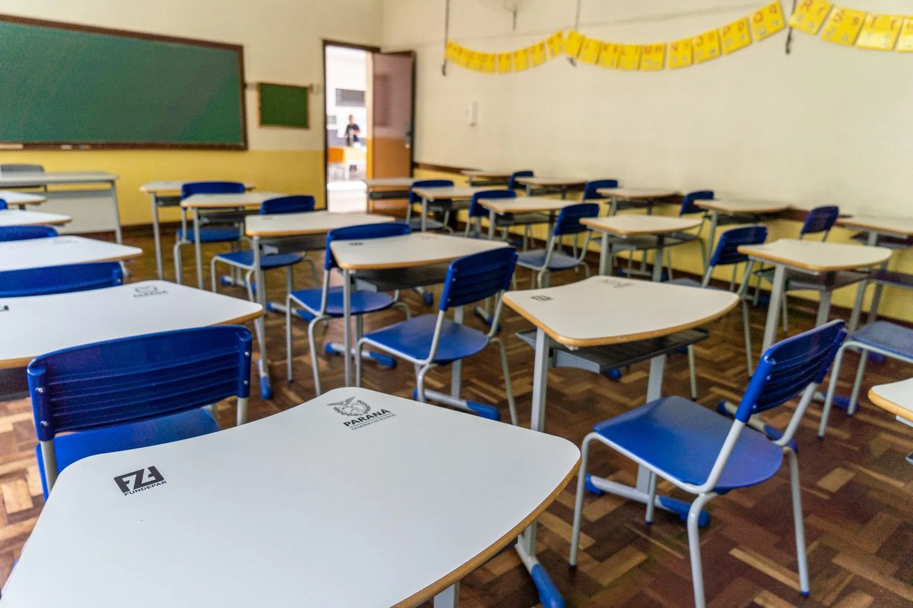 imagem mostra sala de aula vazia, com várias carteiras e alinhadas e um quadro branco ao fundo