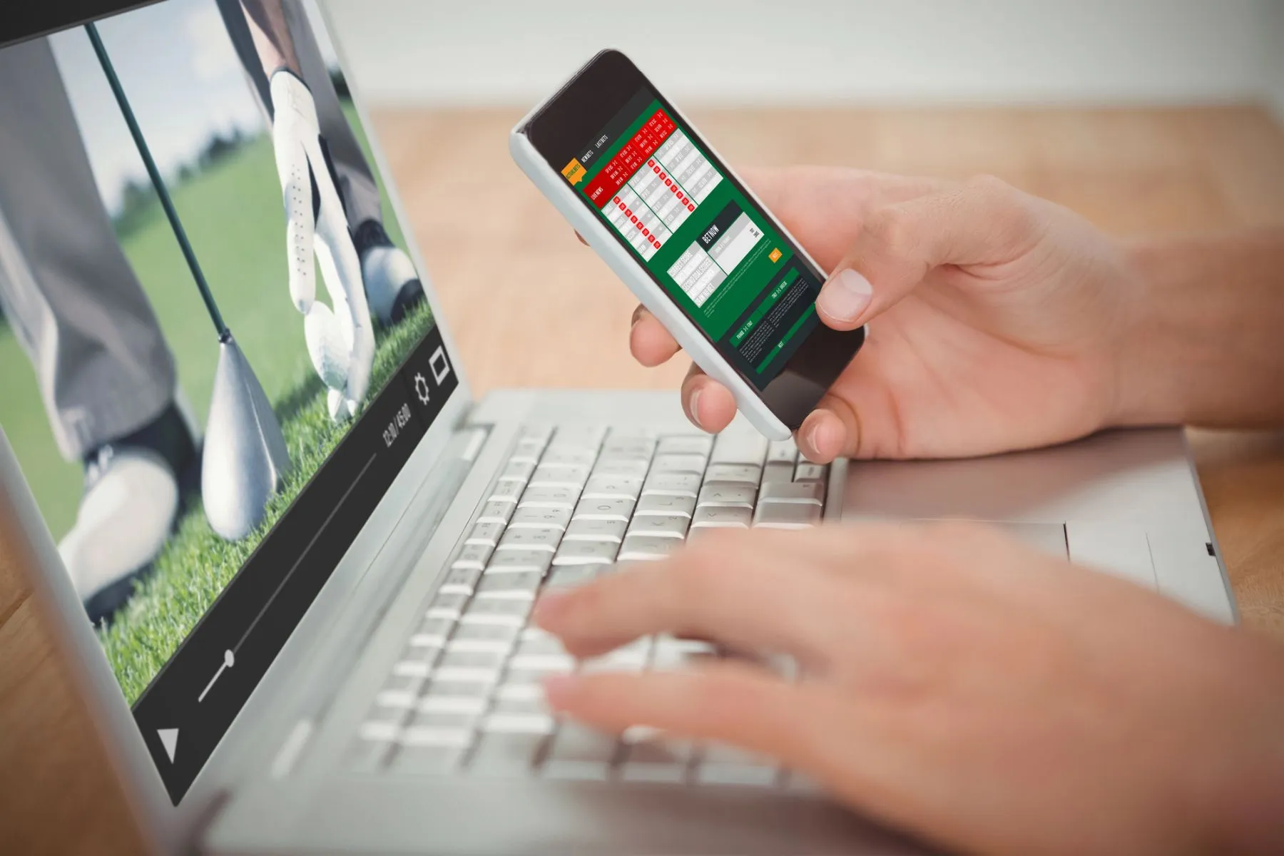 Imagem mostra um notebook com uma partida de golfe na tela, enquanto mãos femininas seguram um celular em um site de apostas