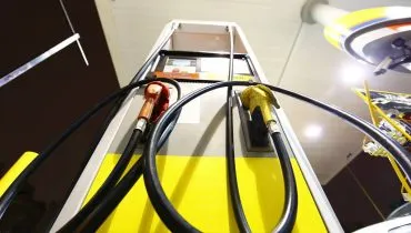 Imagem mostra uma bomba de combustível vista de um ângulo de baixo para cima. É noite na foto e o destaque está nas mangueiras da bomba.