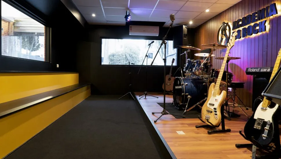 Sala de ensaios de uma escola de música, com palco, guitarras, baixo e bateria. Academia do Rock