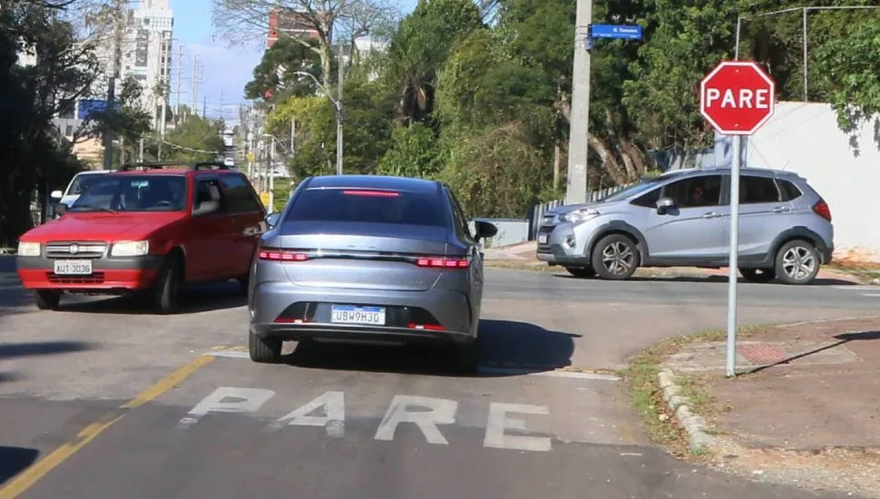 Imagem mostra um cruzamento com carros em Curitiba em um dia de sol.