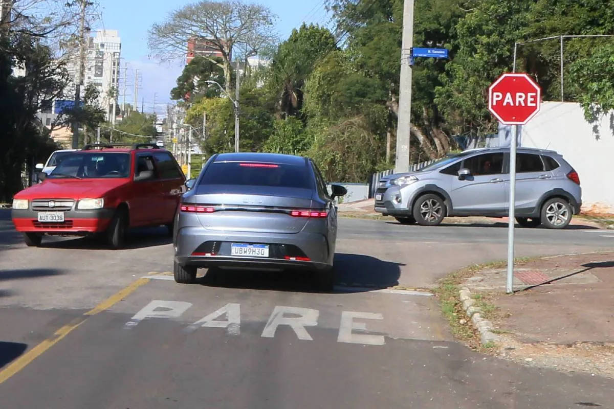 Imagem mostra um cruzamento com carros em Curitiba em um dia de sol.