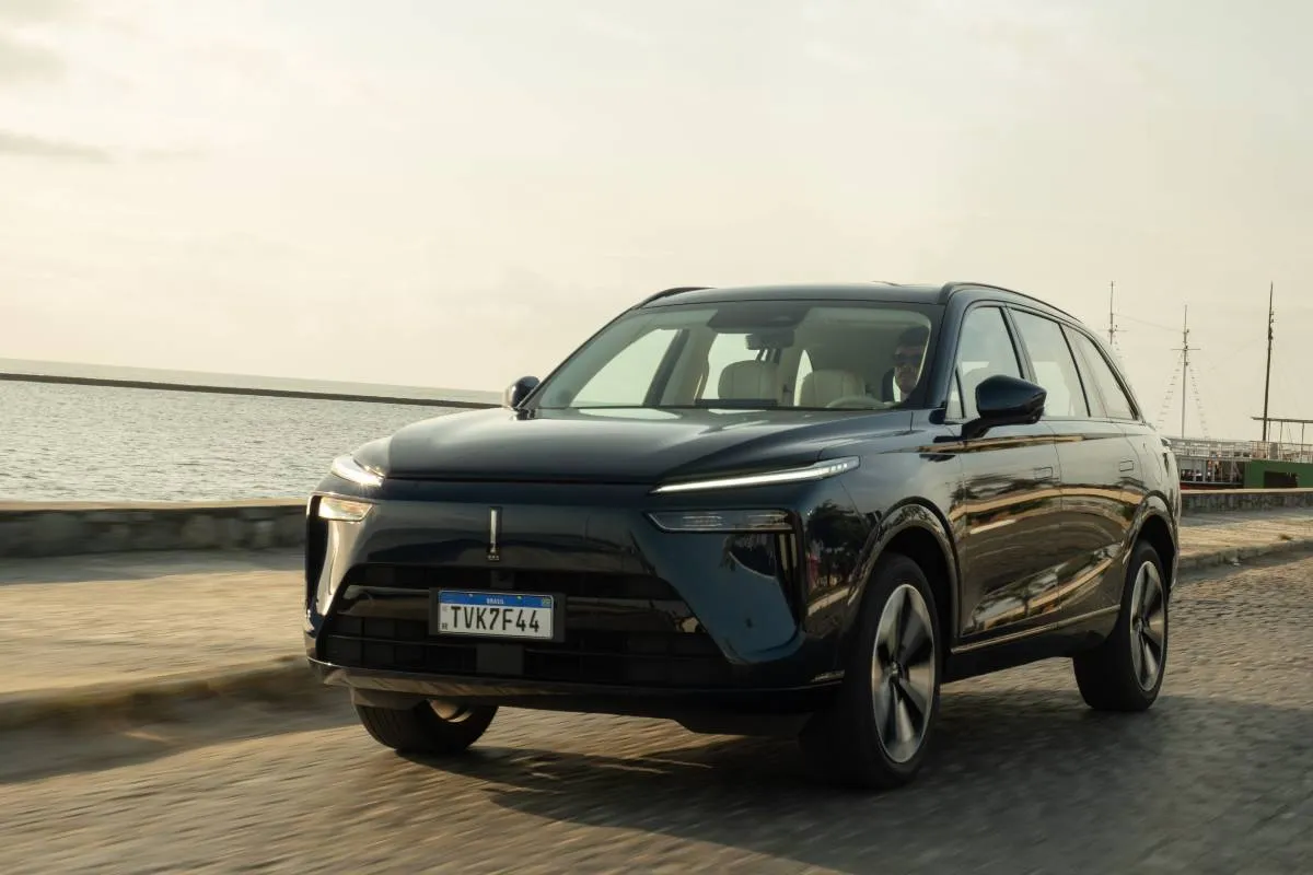 Imagem mostra um SUV preto em uma estrada com mar ao fundo.