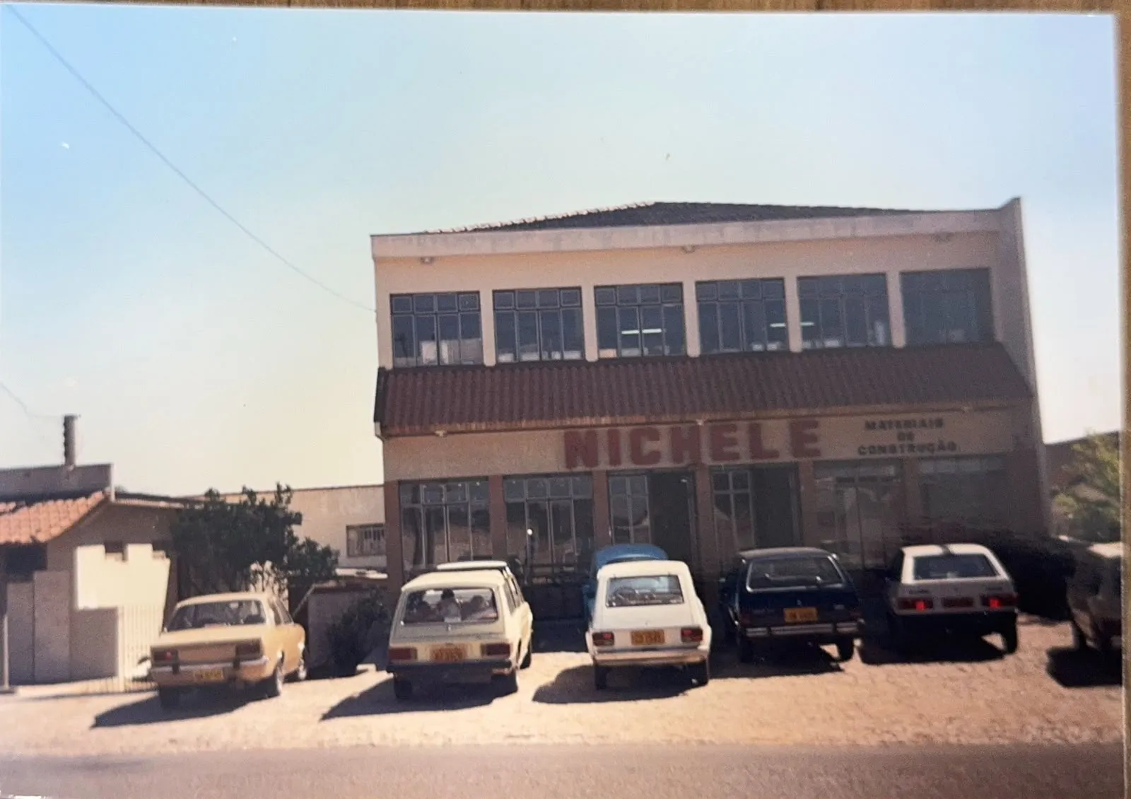 Fachada antiga de loja Nichele com vários carros antigos estacionados na frente / Nichele Materiais Para Construção completa 50 anos
