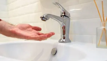 Imagem mostra uma pessoa com a mão debaixo de uma torneira sem água.