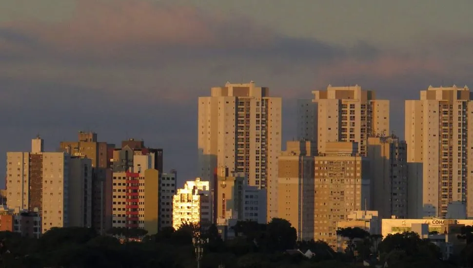 Imagem mostra uma sequência de prédios com nuvens carregadas ao fundo.