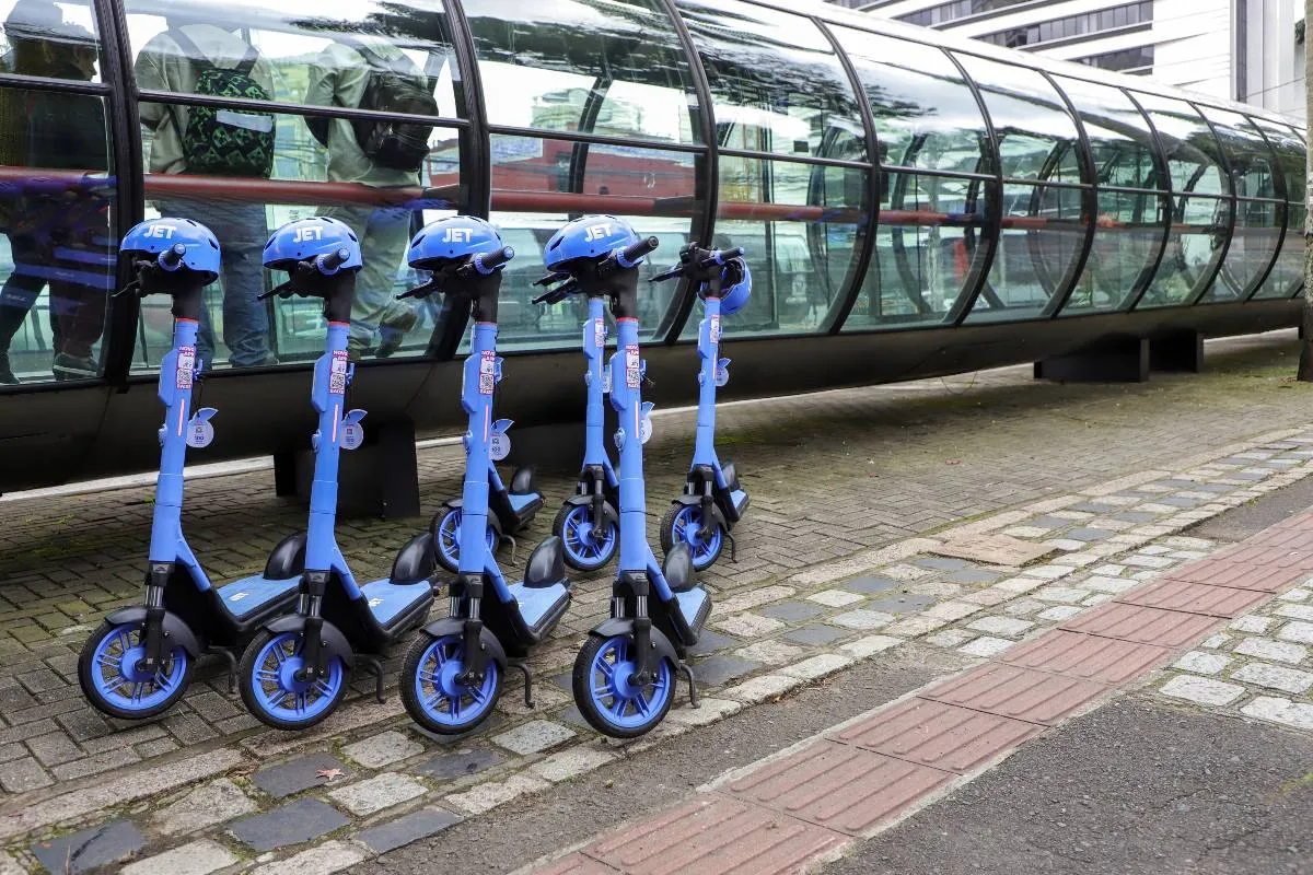 Imagem mostra patinetes azuis na frente de uma estação tubo em Curitiba.