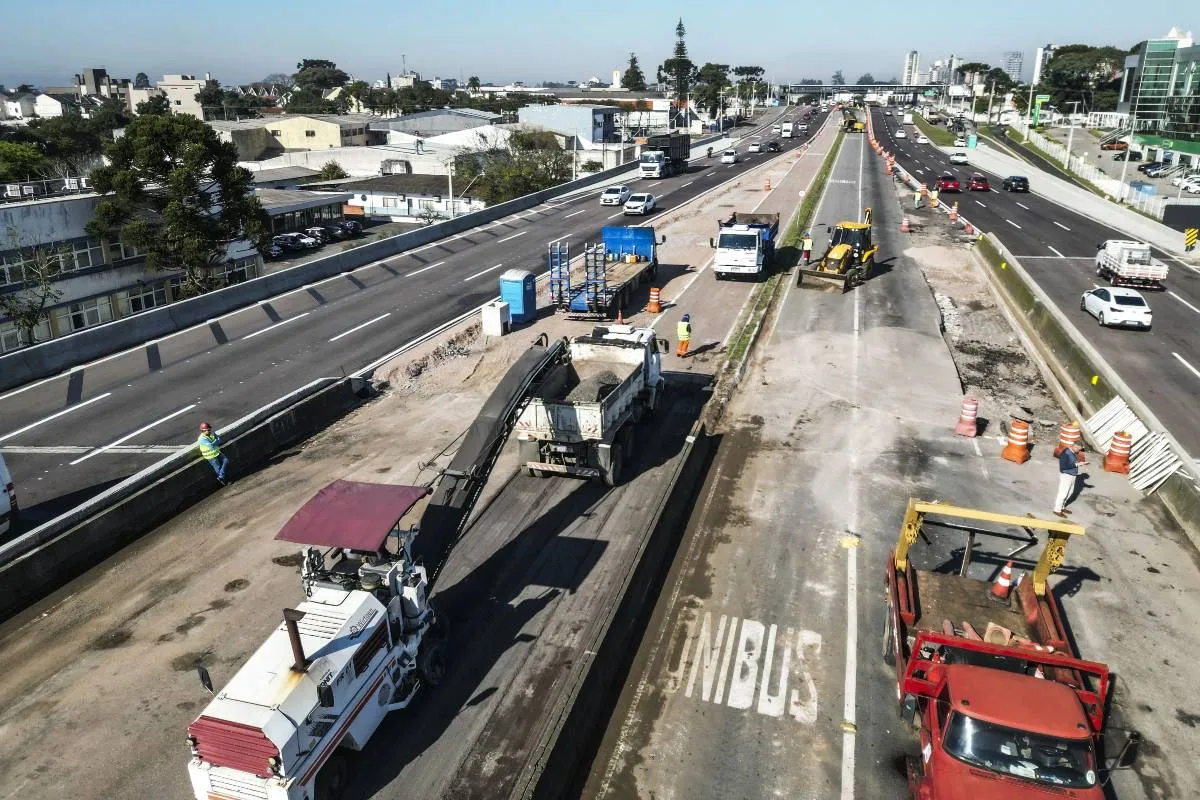Imagem de drone mostra as obras no complexo Taruma, com máquinas trabalhando, muitos cones, caminhões e carros passando nas faixas das extremidades.