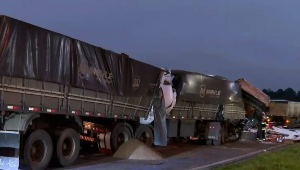 Imagem no amanhecer motra dois caminhões acidentados na BR-277, em Campo Largo. Um deles está com vazamento de carga (soja) no asfalto e a cabine completamente destruída.