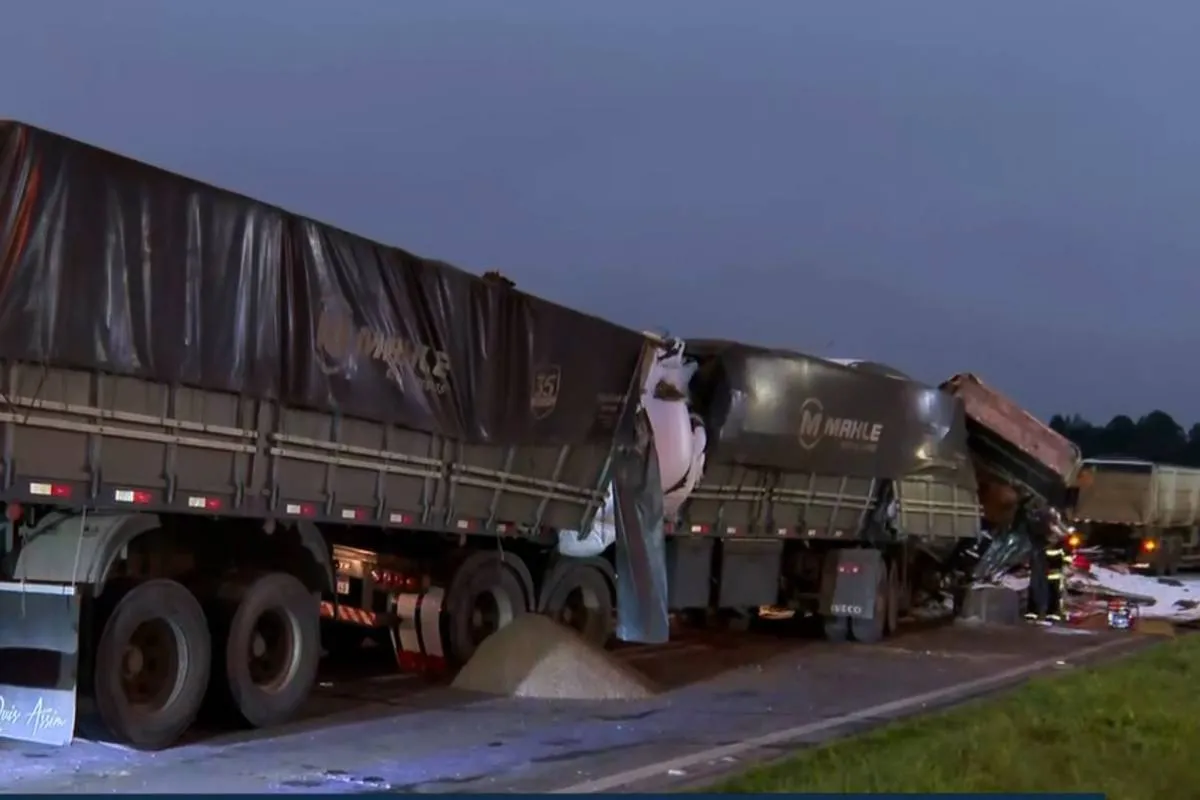 Imagem no amanhecer motra dois caminhões acidentados na BR-277, em Campo Largo. Um deles está com vazamento de carga (soja) no asfalto e a cabine completamente destruída.