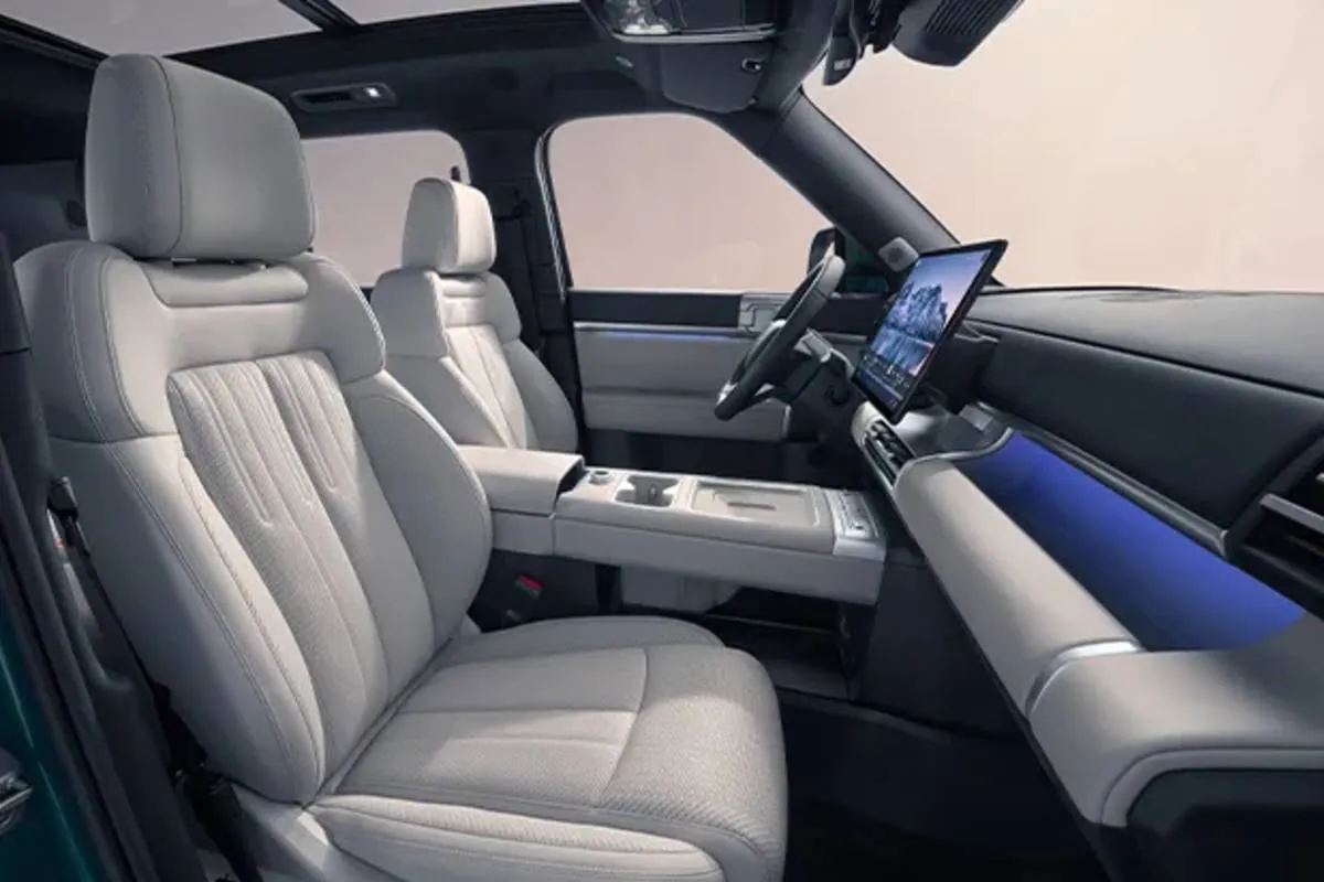 Imagem mostra o interior do BYD TI 7 com bancos brancos e tela multimídia de 15,6 polegadas.