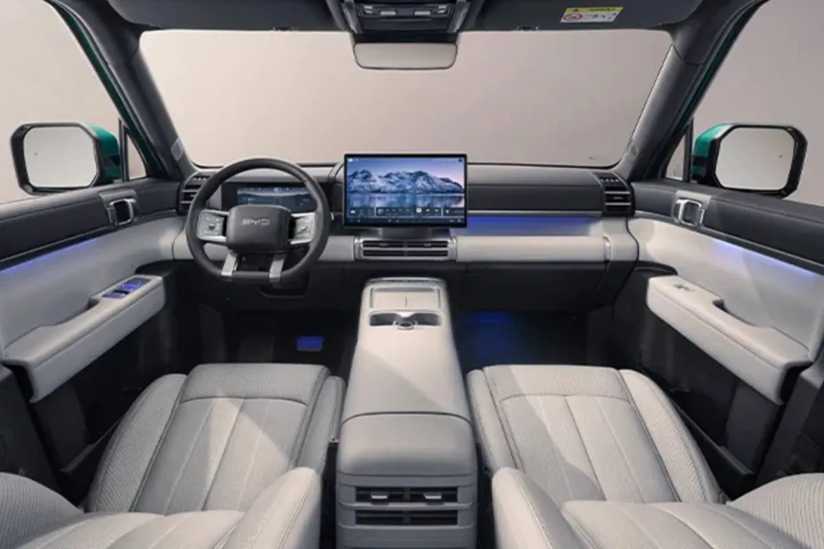 Imagem mostra o interior do BYD TI 7 com bancos brancos e tela multimídia de 15,6 polegadas.
