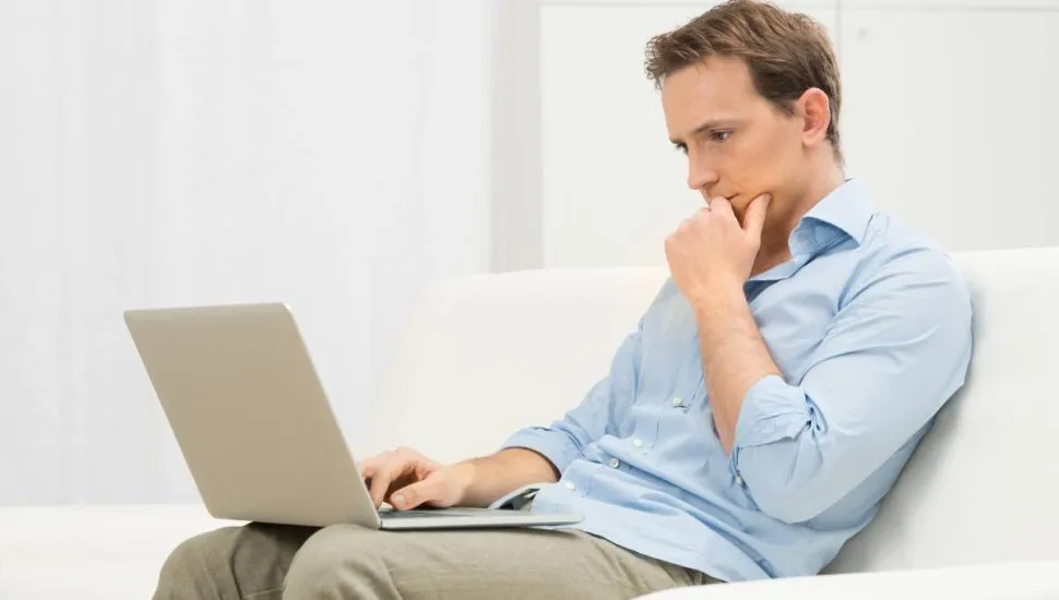 Imagem mostra um homem pensando com um notebook no colo.