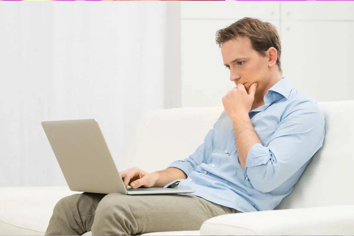 Imagem mostra um homem pensando com um notebook no colo.