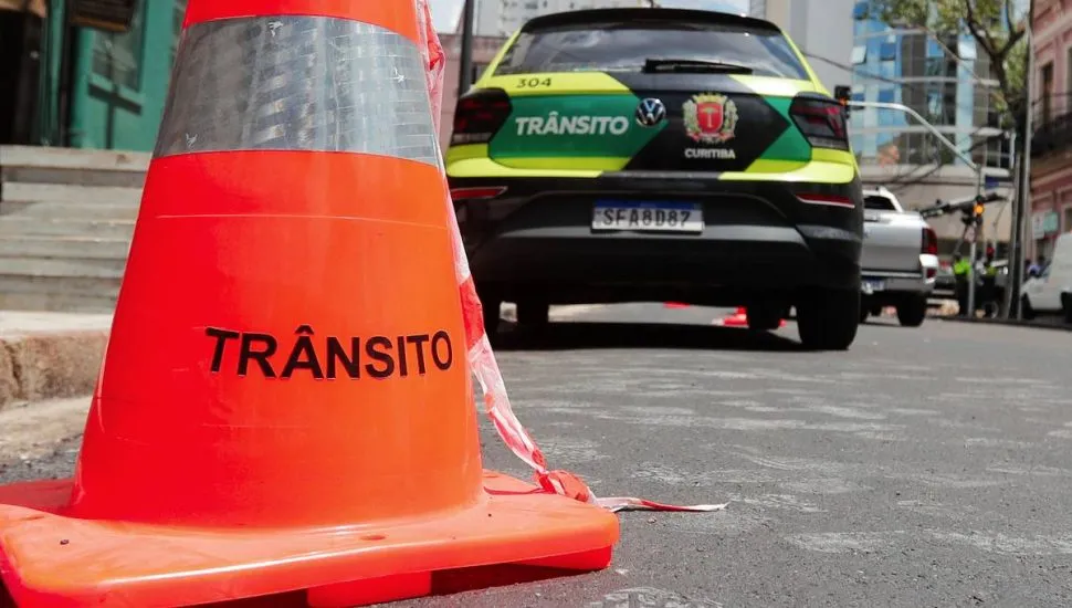 Imagem mostra um cone com o escrito "Trânsito" e uma viatura da Setran ao fundo. A viatura tem as cores verde limão e preto.