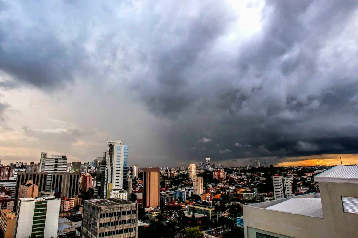 Imagem mostra Curitiba em uma visão ampla, com uma grande nuvem de tempestade se aproximando.