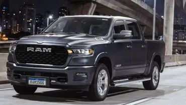 Imagem mostra a nova RAM 1500 big horn. No detalhe a frente da nova picape de grande porte da marca na cor azul marinho, com uma grade robusta escrito RAM em uma pista durante a noite.