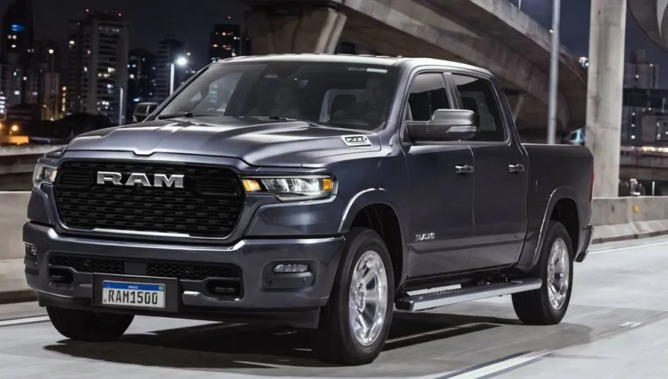 Imagem mostra a nova RAM 1500 big horn. No detalhe a frente da nova picape de grande porte da marca na cor azul marinho, com uma grade robusta escrito RAM em uma pista durante a noite.
