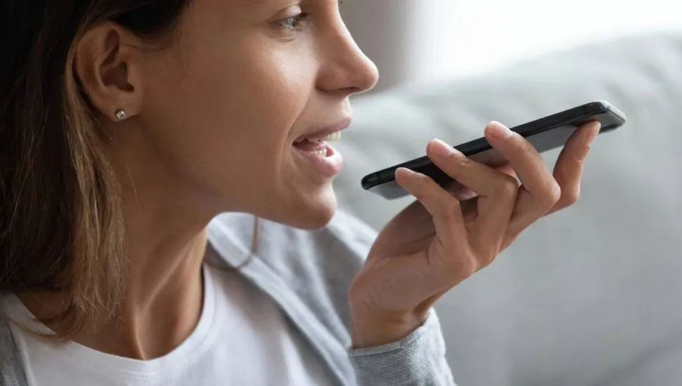 Imagem mostra uma mulher usando um celular para mandar mensagem de áudio, uma das ferramentas disponíveis no WhatsApp.