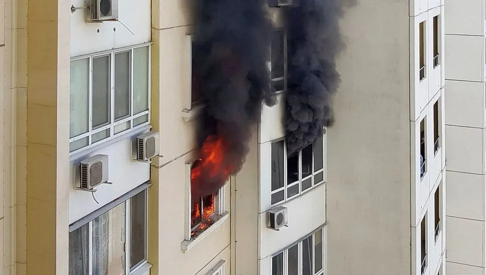 Imagem mostra visão lateral de um edifício, cum fogo saindo de uma das janelas do prédio e uma grande coluna de fumaça