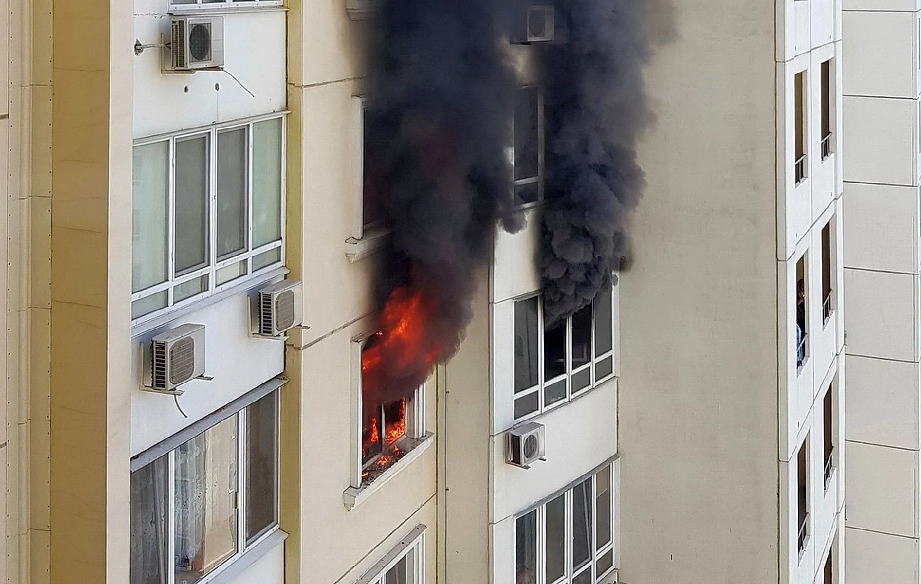 Imagem mostra visão lateral de um edifício, cum fogo saindo de uma das janelas do prédio e uma grande coluna de fumaça