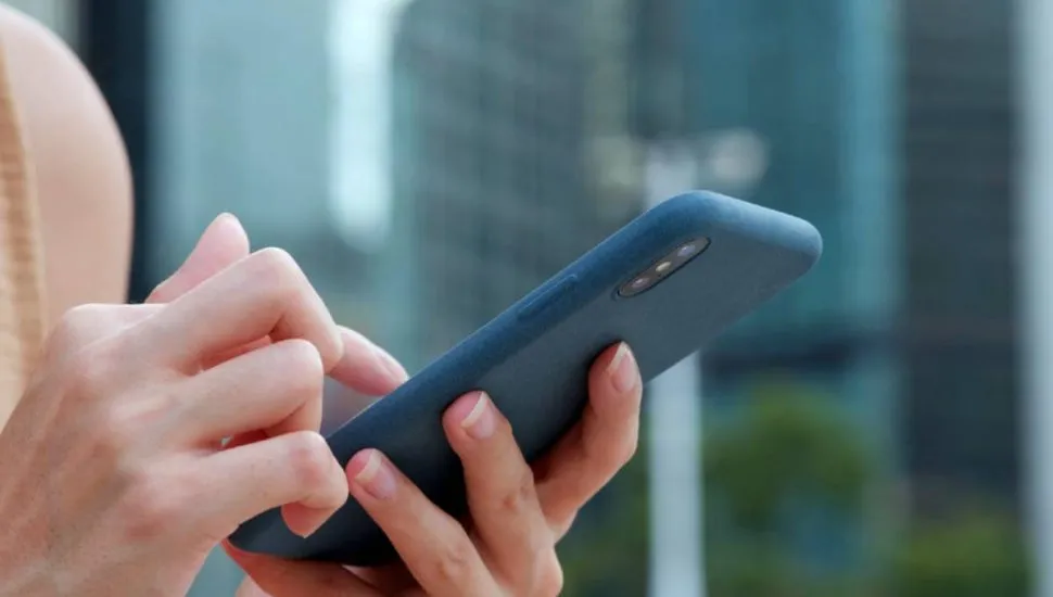 Imagem mostra uma pessoa segurando um celular com uma capinha azul com prédios ao fundo.