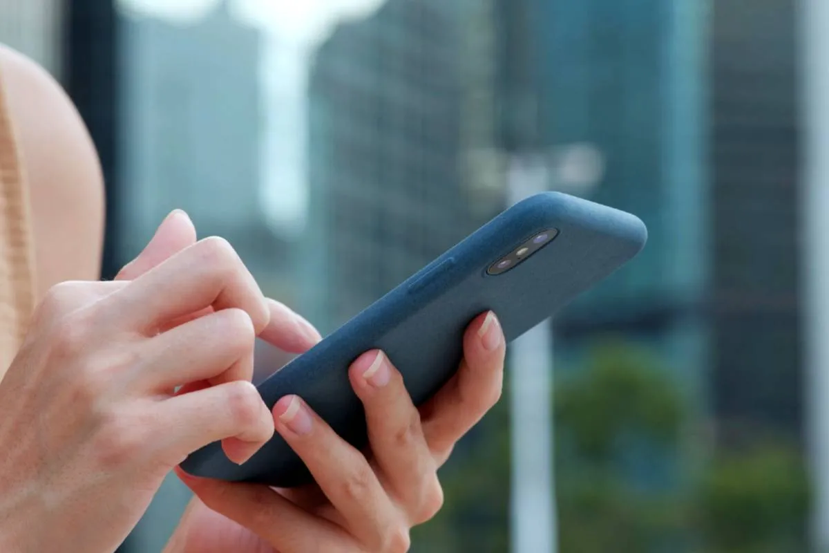 Imagem mostra uma pessoa segurando um celular com uma capinha azul com prédios ao fundo.