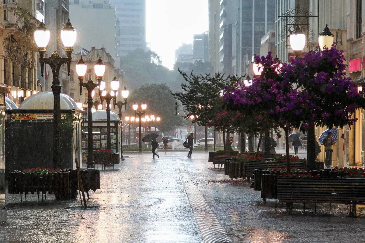 Imagem mostra o centro de Curitiba em um dia de chuva intensa, com pessoas de guarda chuva e piso todo olhado.
