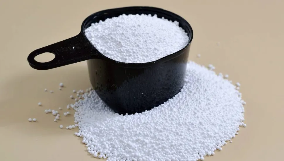 Imagem mostra um copo medidor com percarbonato de sódio em cima de uma mesa bege.